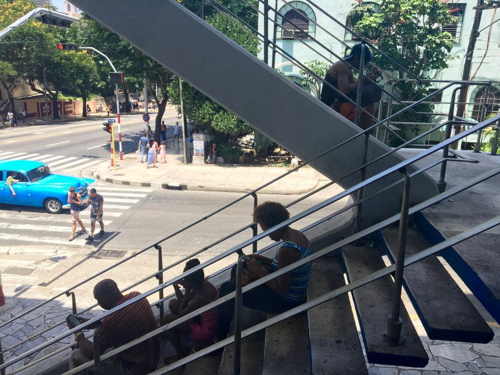 Four women sit on steps of an outdoor stairway looking at their phones